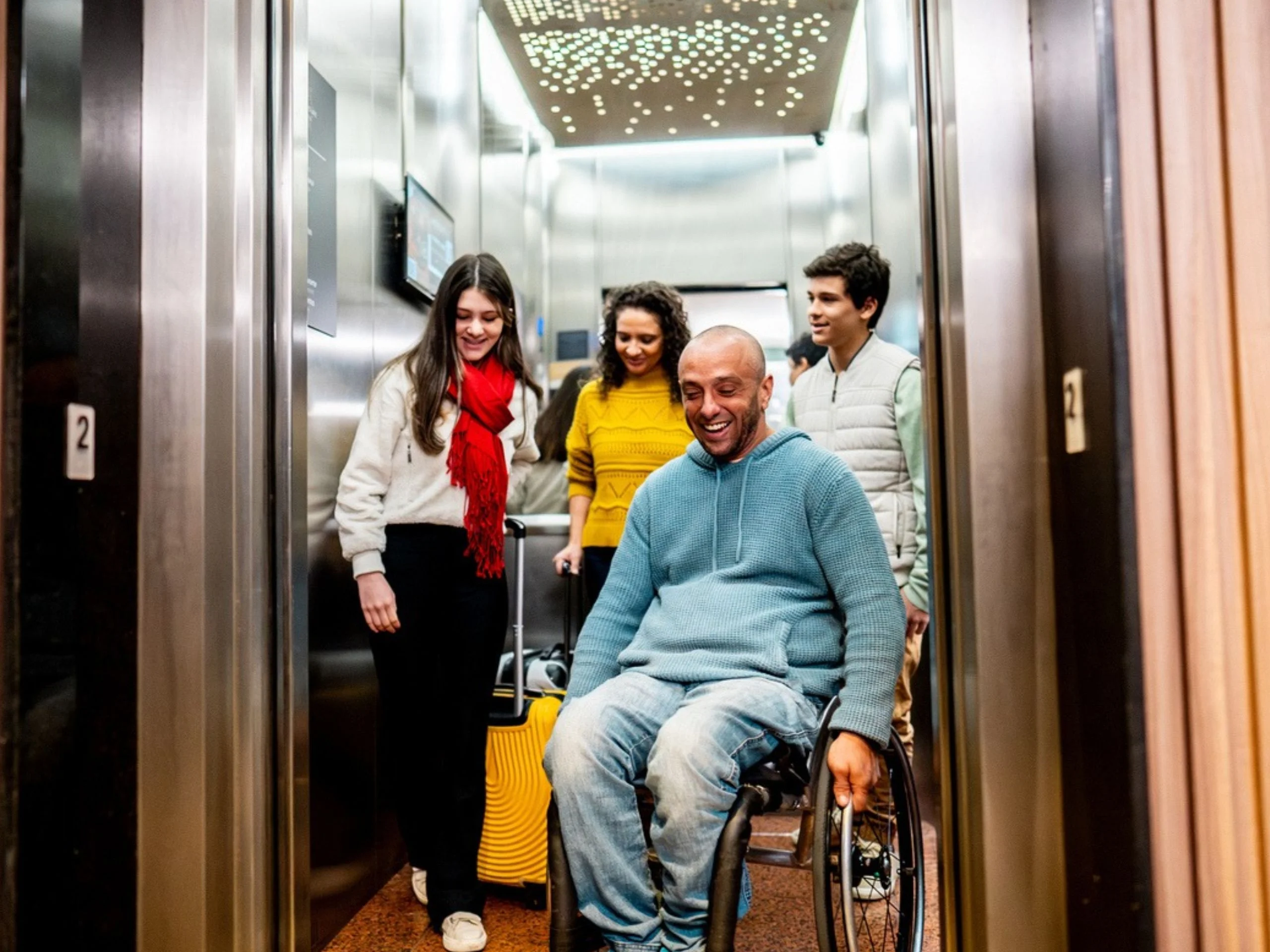 Hombre en silla de ruedas saliendo de un ascensor con sus vecinos