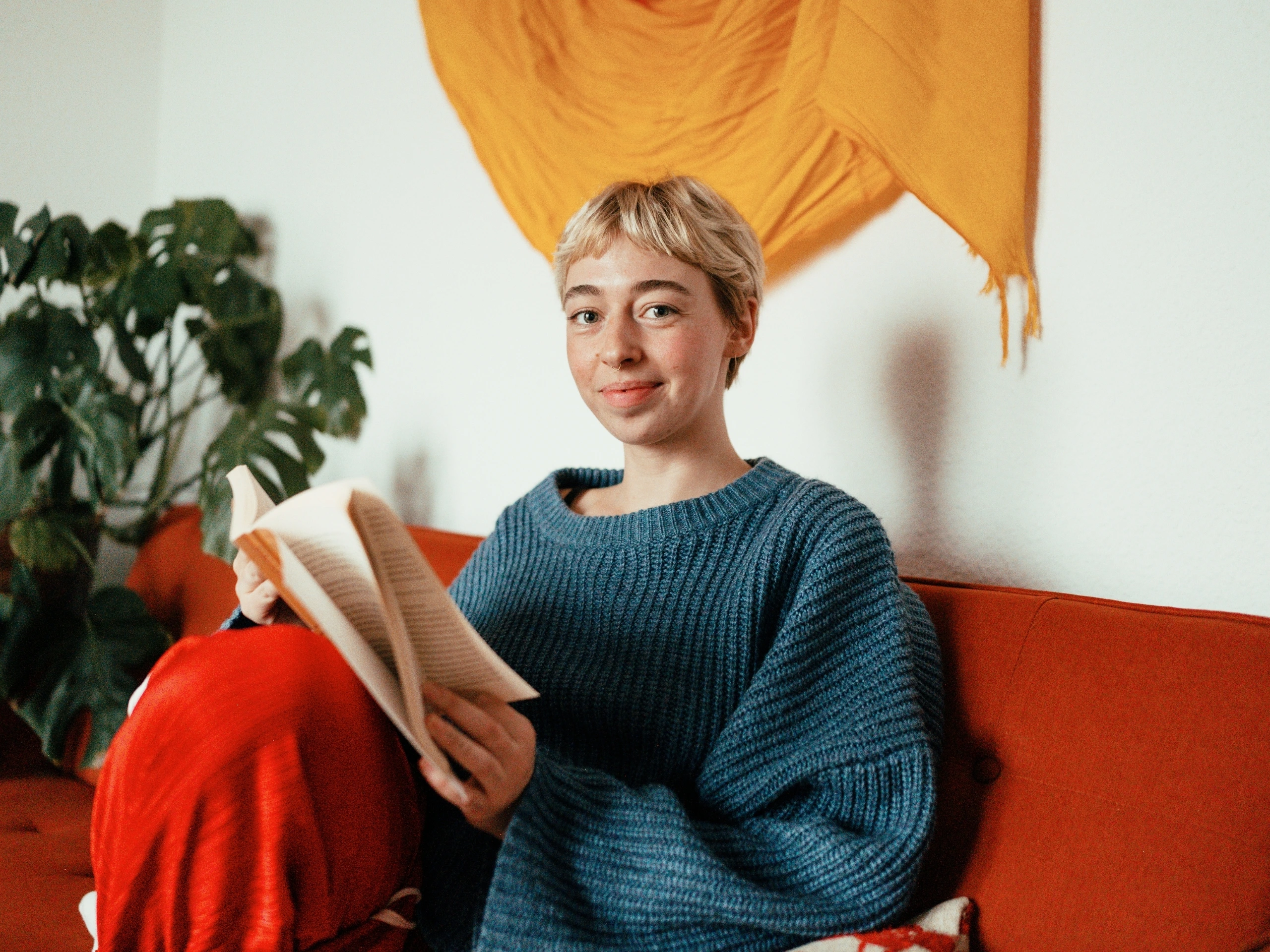 Chica joven leyendo un libro sentada en el sofá de su piso alquilado