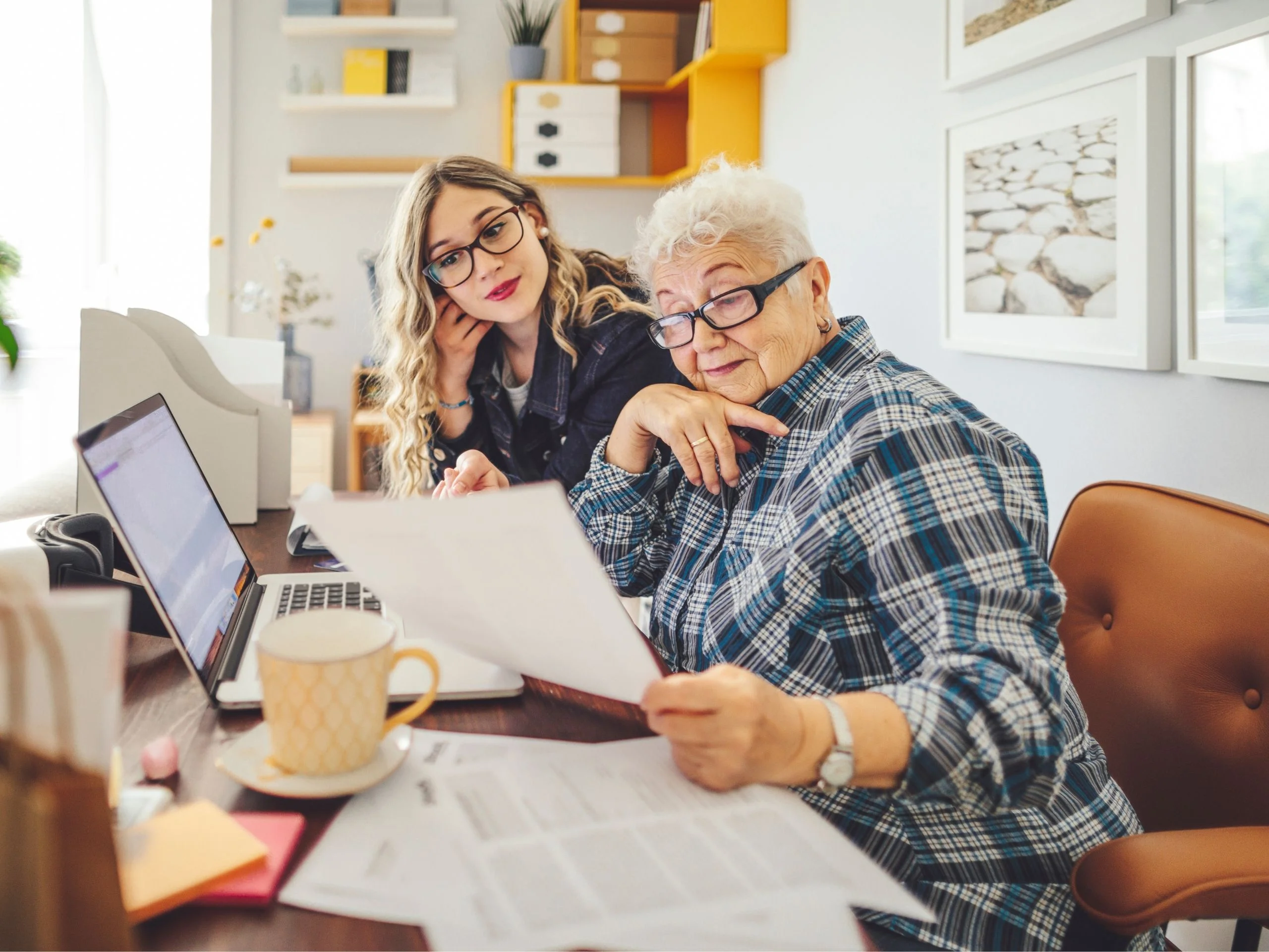 Mujer mayor y mujer joven mirando recibos y anotando en un portátil