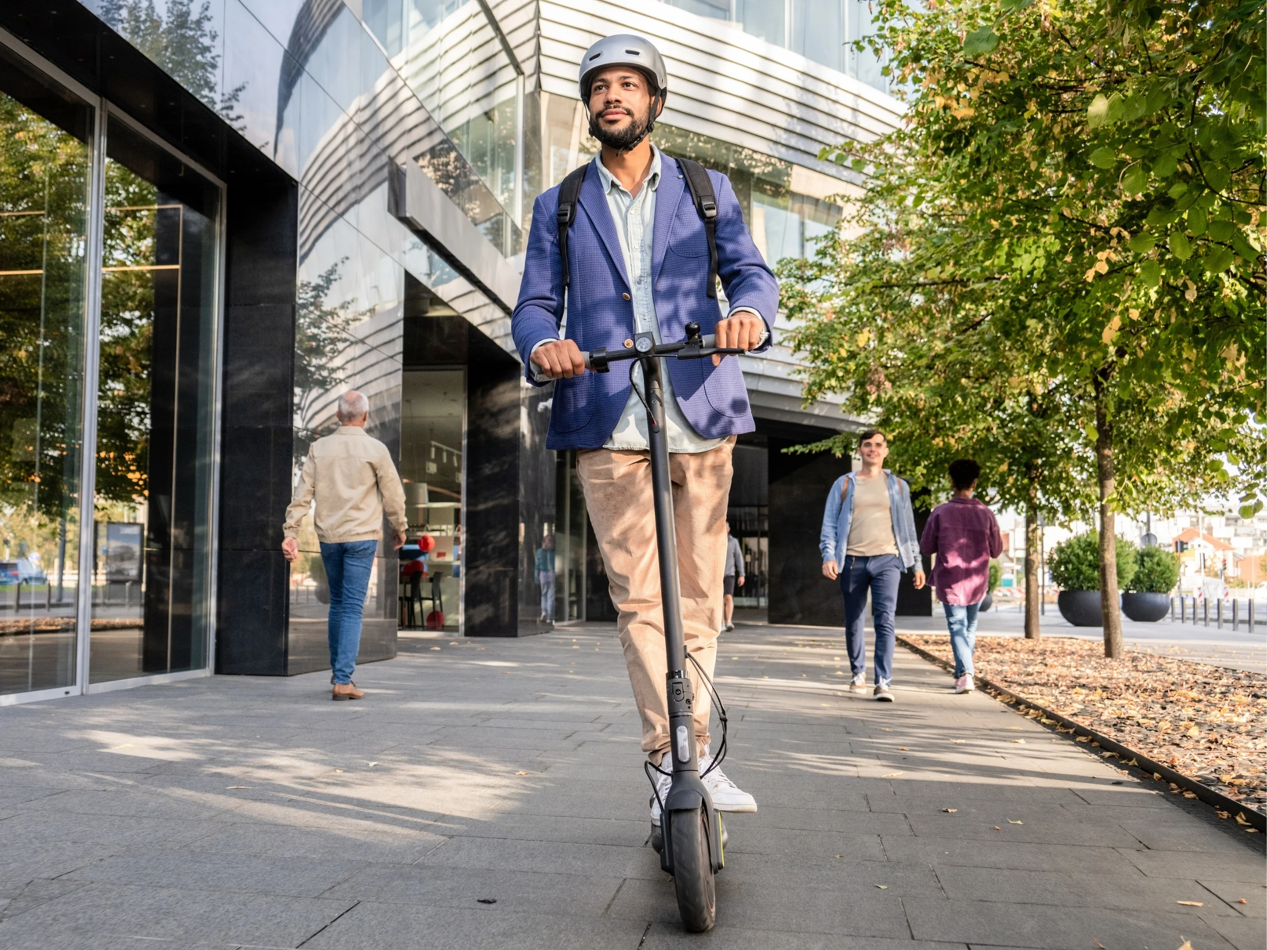 Hombre de negocios con casco y mochila circulando con un patinete