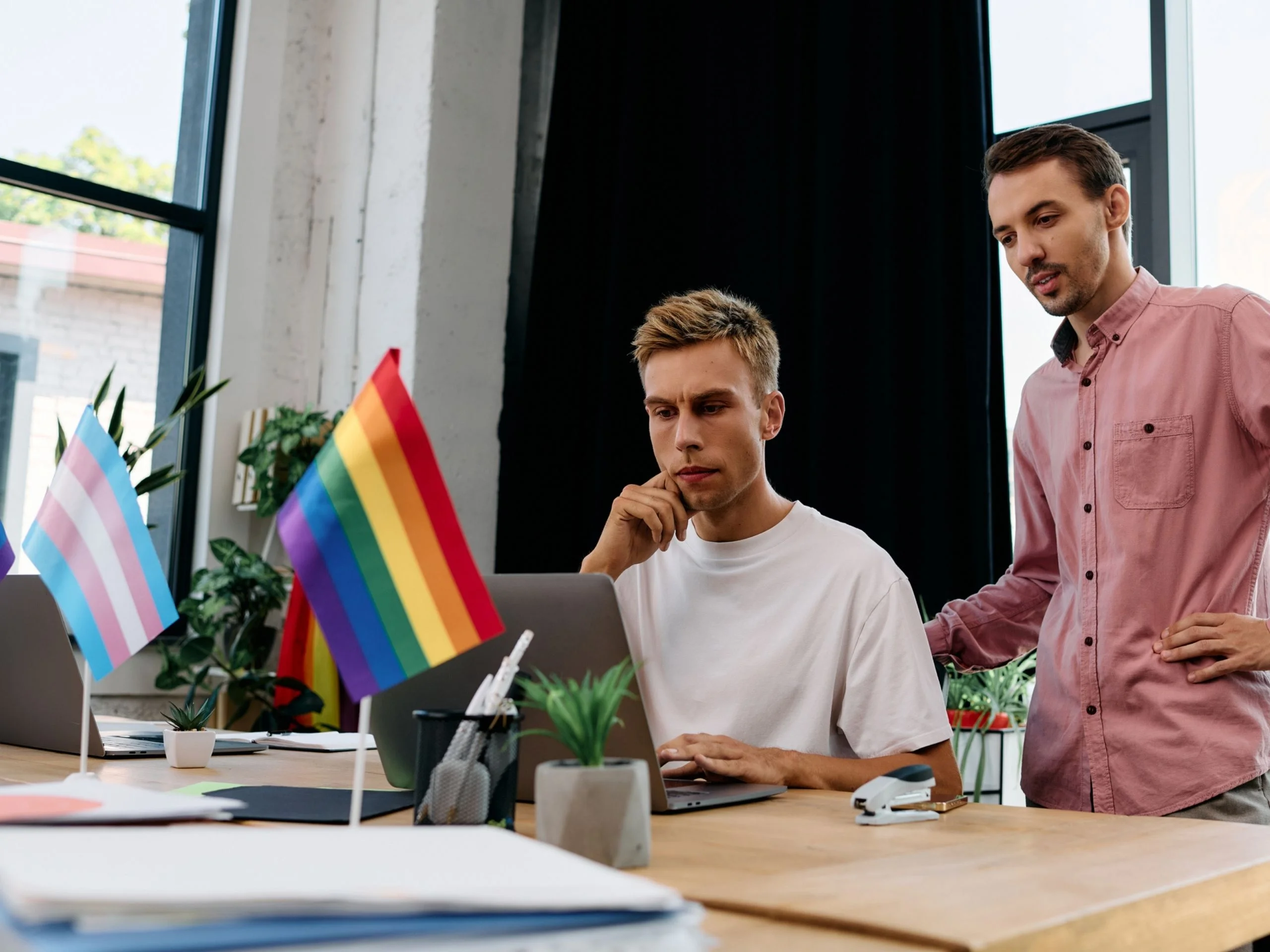 Dos hombres en el despacho, con mesa con banderas trans y lgbti