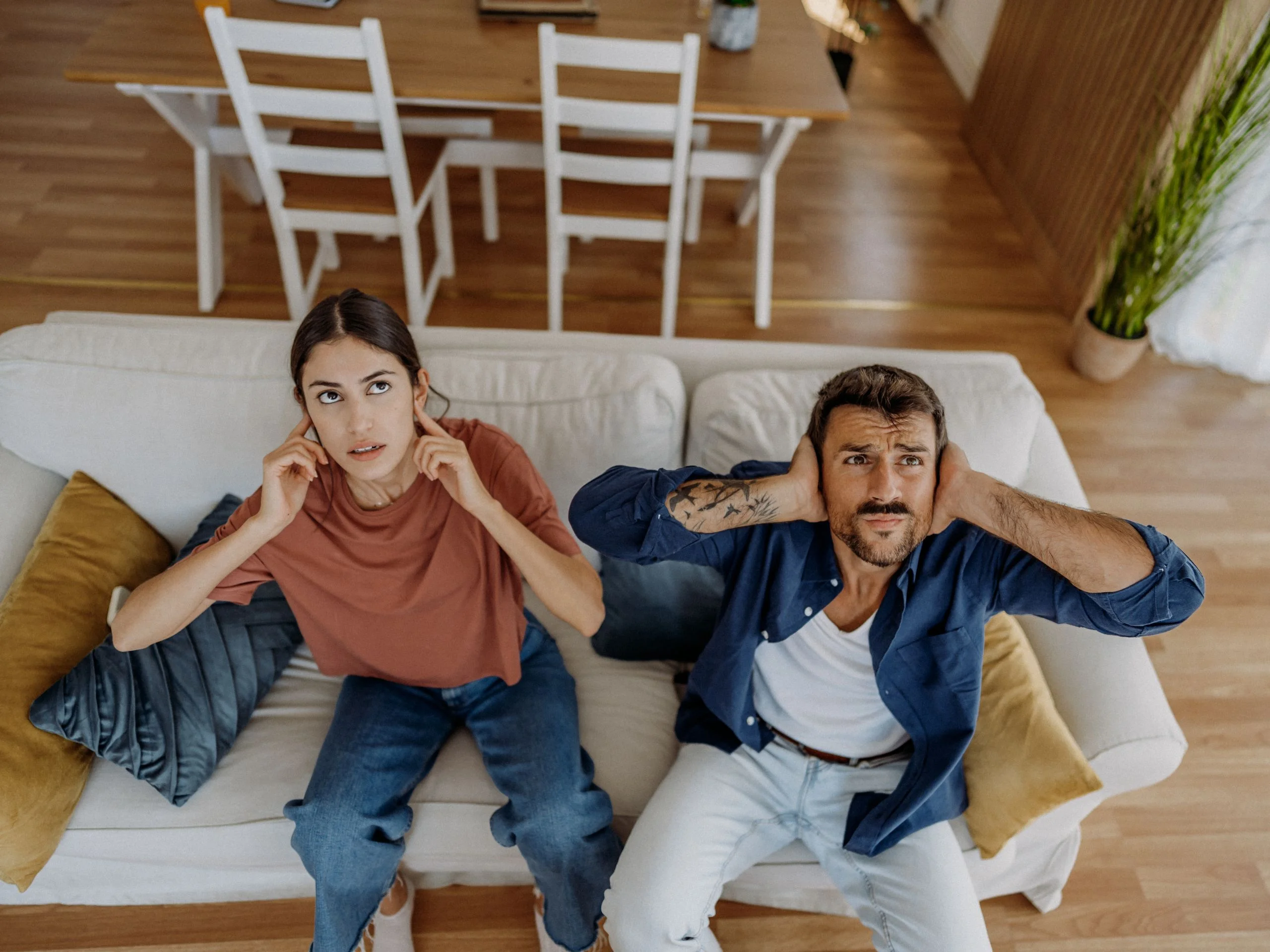 Pareja en el sofá de casa tapándose las orejas por los ruidos de los vecinos