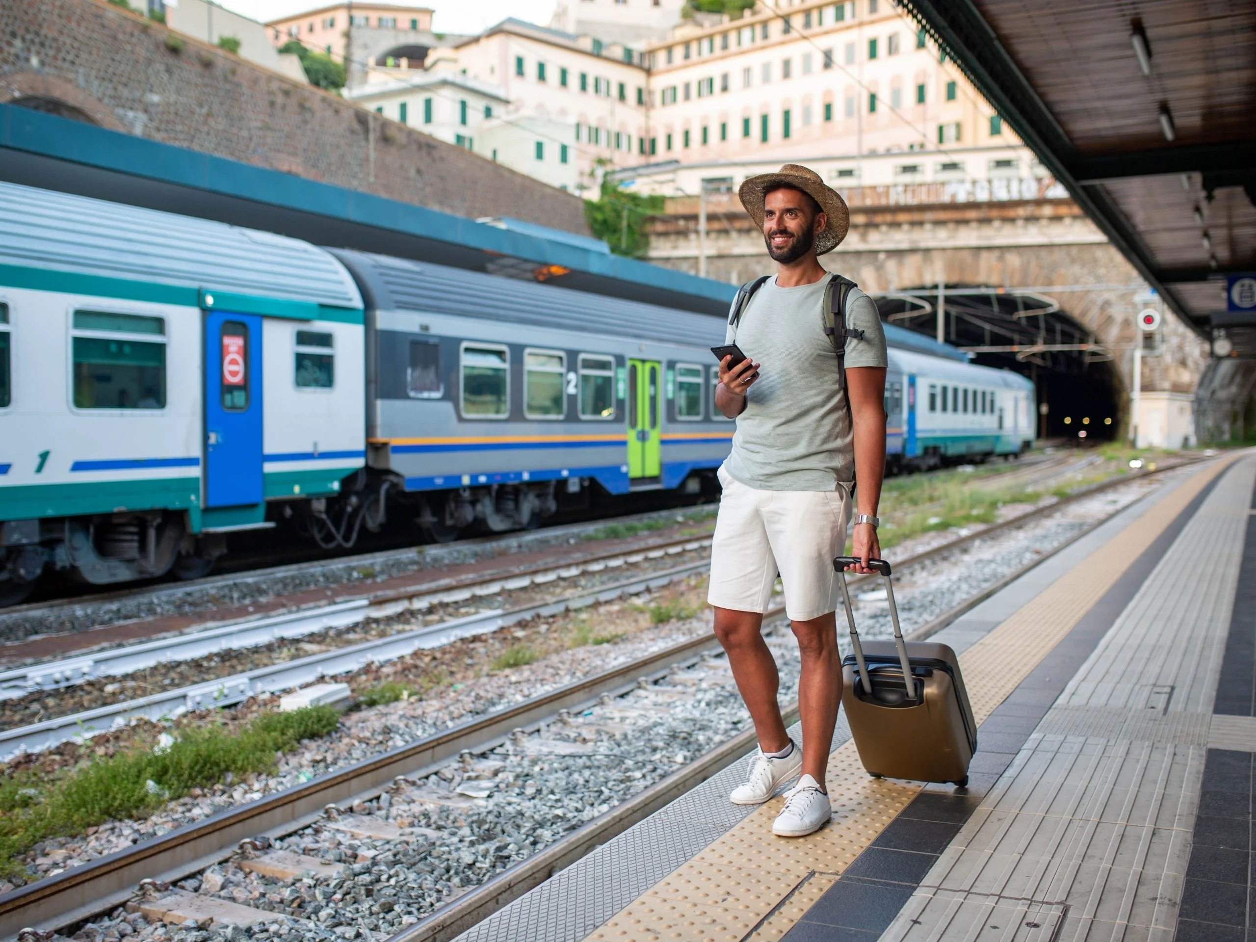 Hombre con maleta esperando sonriente en andén de tren