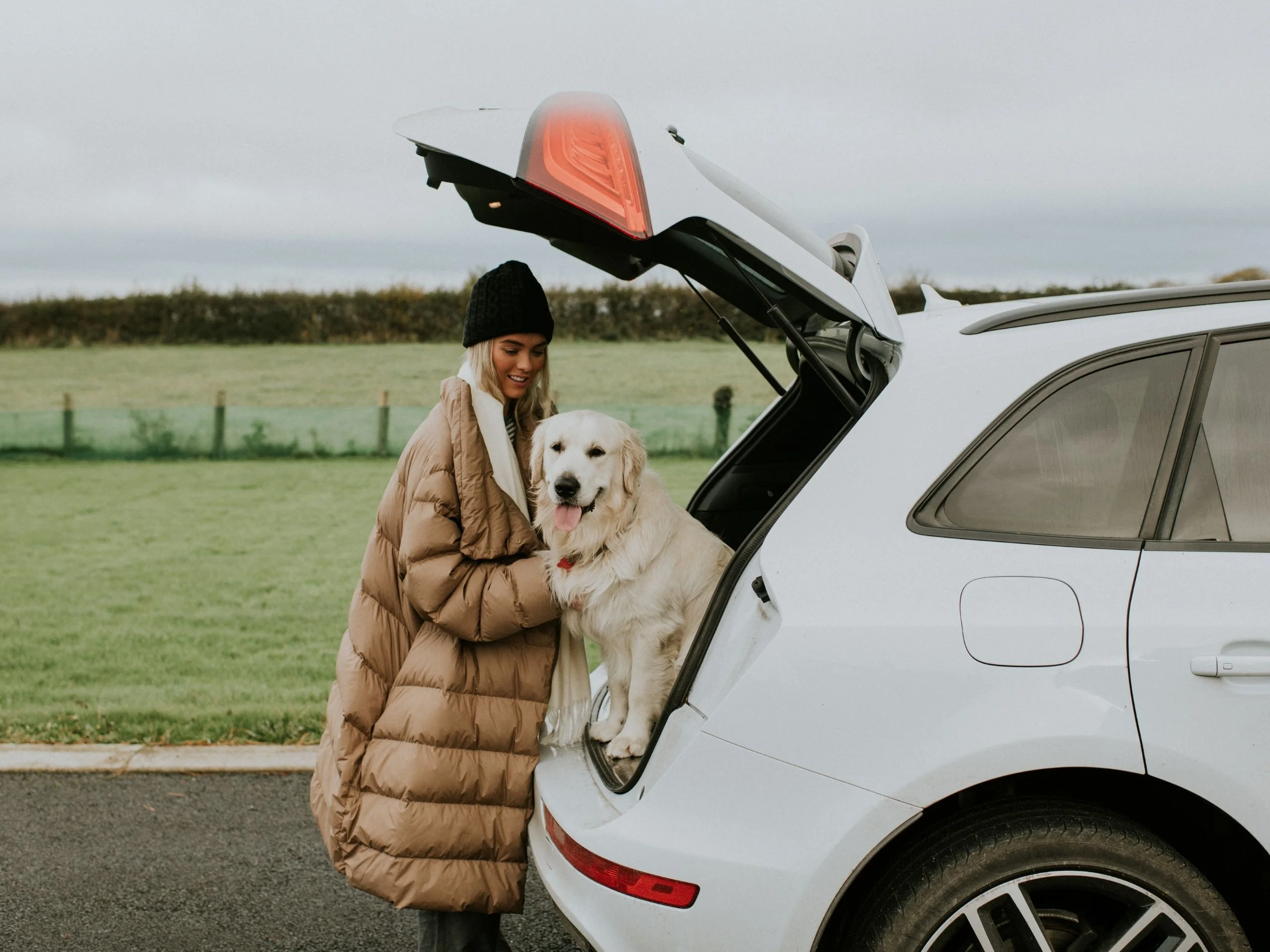 Mujer abrazando a su perro, sentado en el maletero del coche