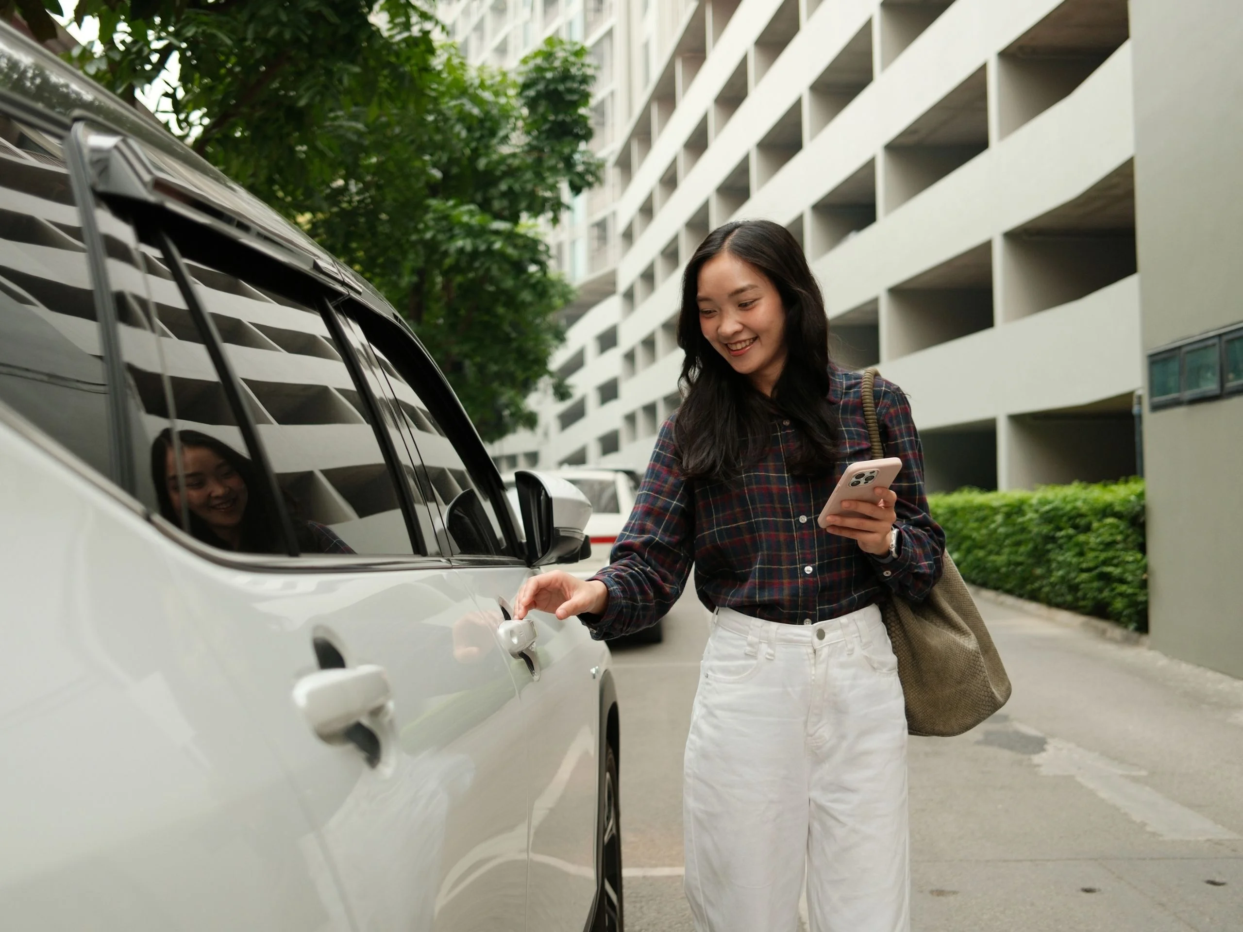 Mujer sujetando el móvil abriendo la puerta del coche, navegando por la app de coche compartido en un aparcamiento urbano