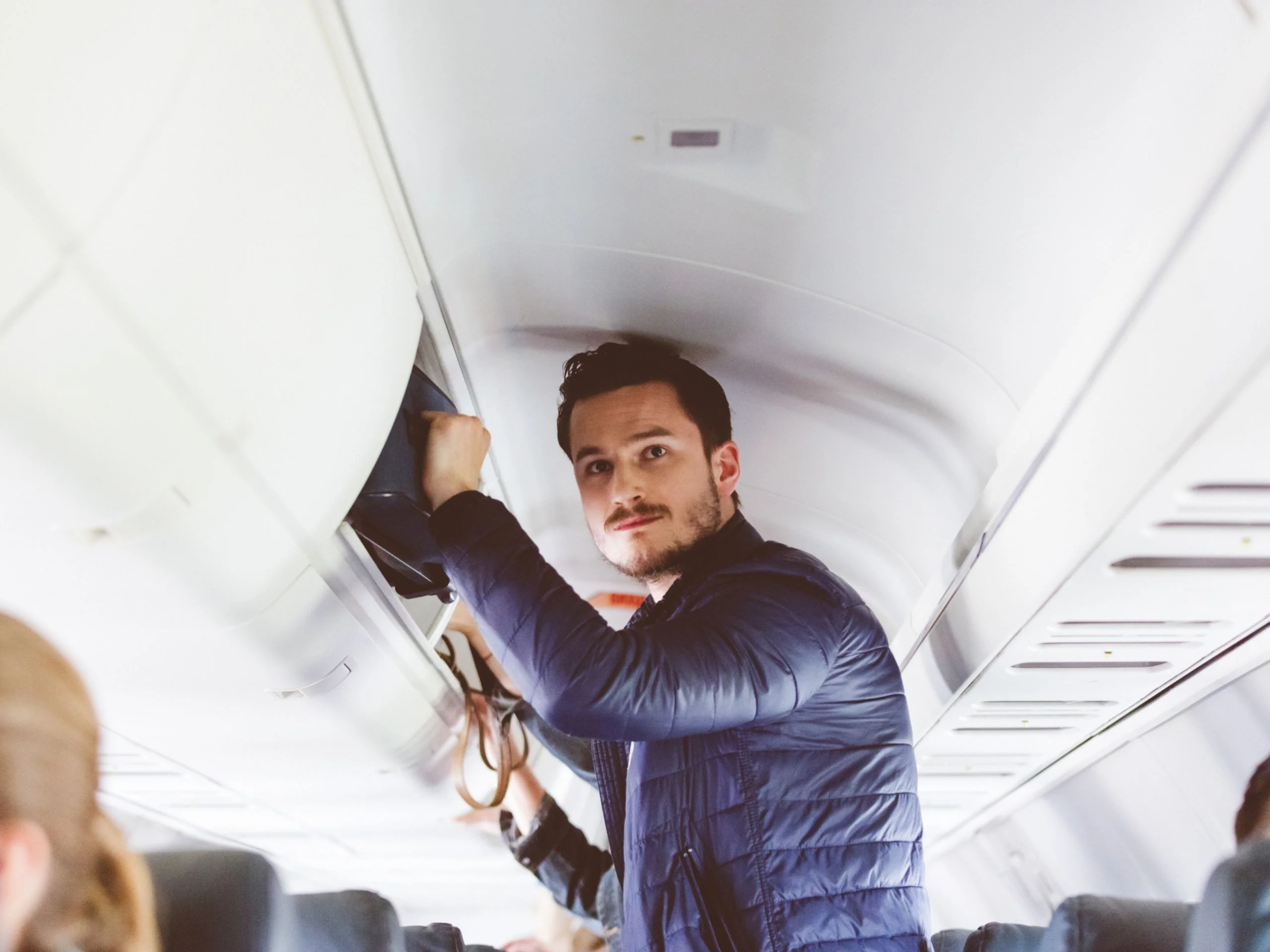 Hombre joven poniendo su maleta en el portaequipajes del avión