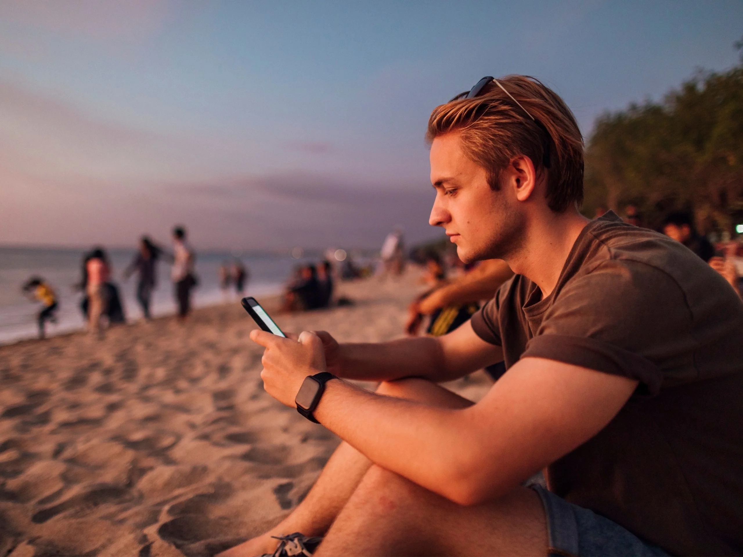 Hombre joven en la playa mirando el móvil