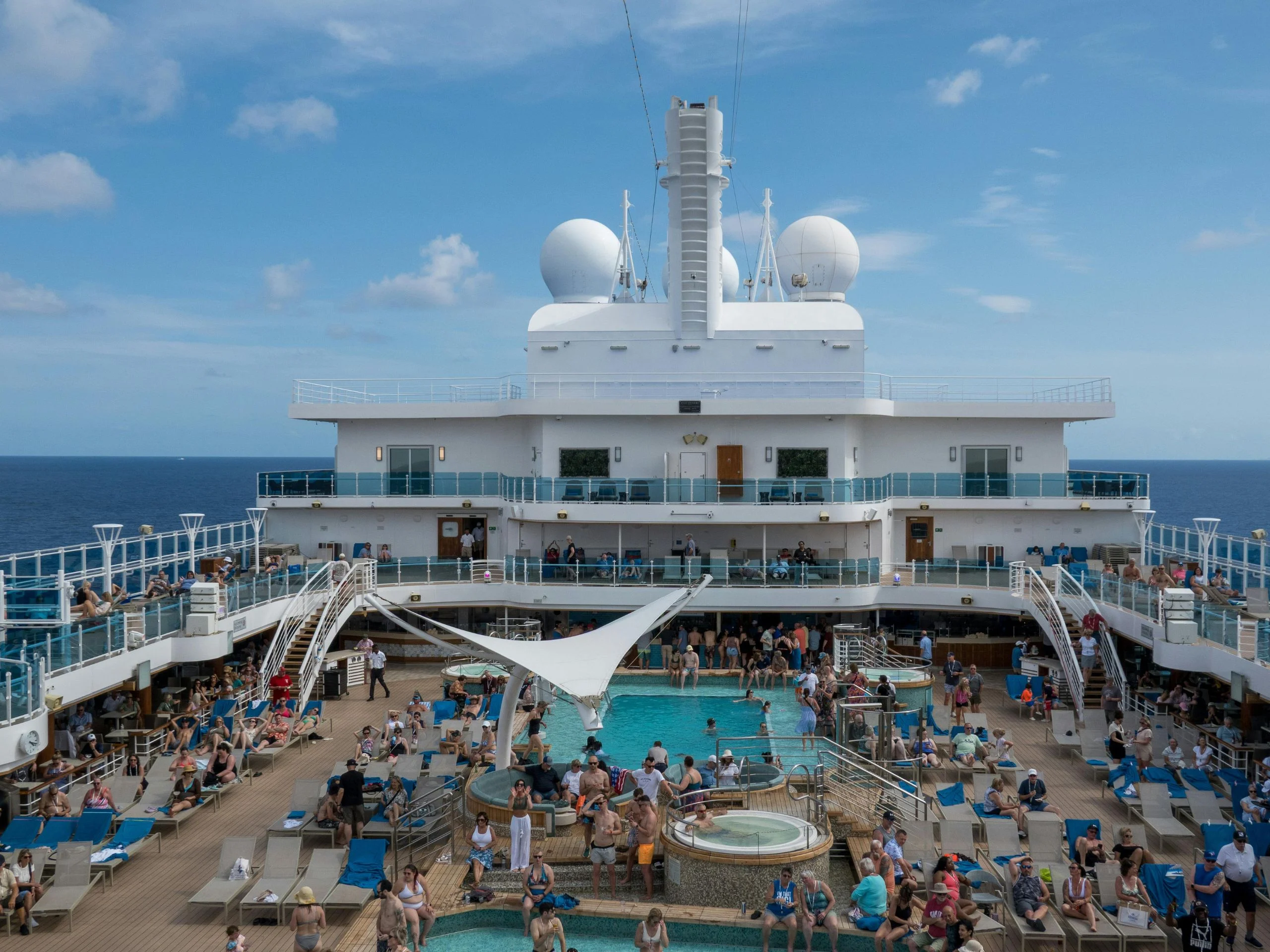 Relajante escena en la cubierta de un crucero con piscina y bañistas disfrutando de un día soleado en el mar.