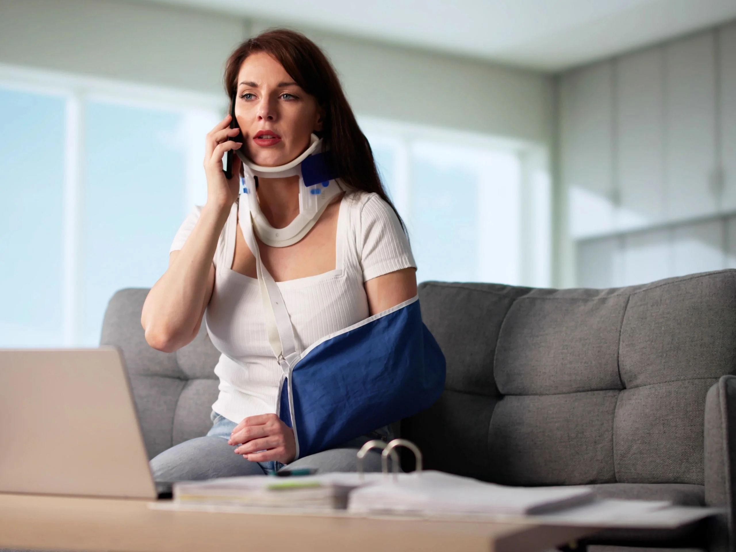 Una mujer lesionada con un brazo roto en el sofá hablando por teléfono