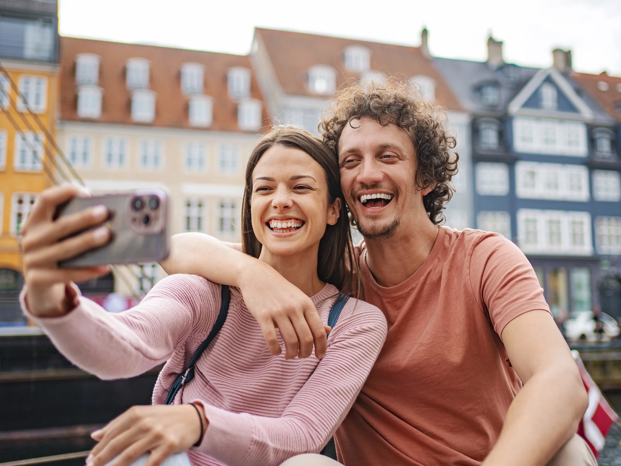 Pareja sonriente tomándose un selfie frente a edificios históricos de Copenhaguen.