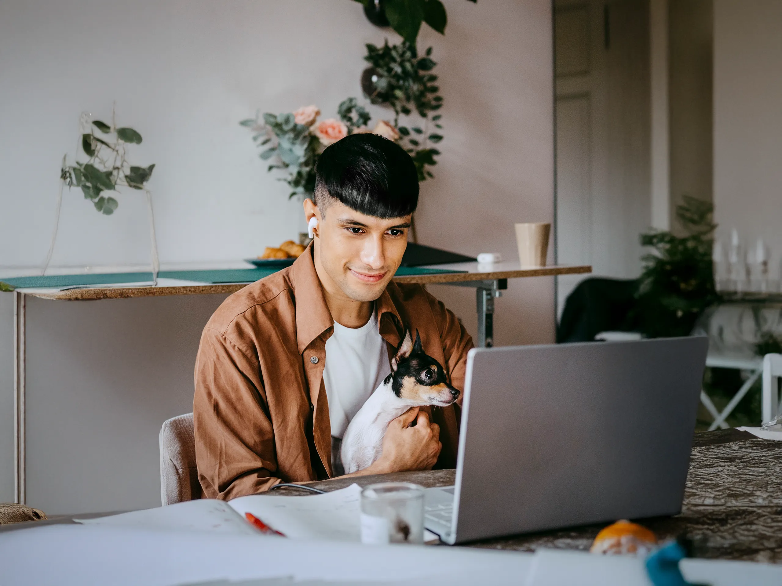 Un hombre trabaja con una computadora portátil mientras sostiene un pequeño perro en sus brazos.