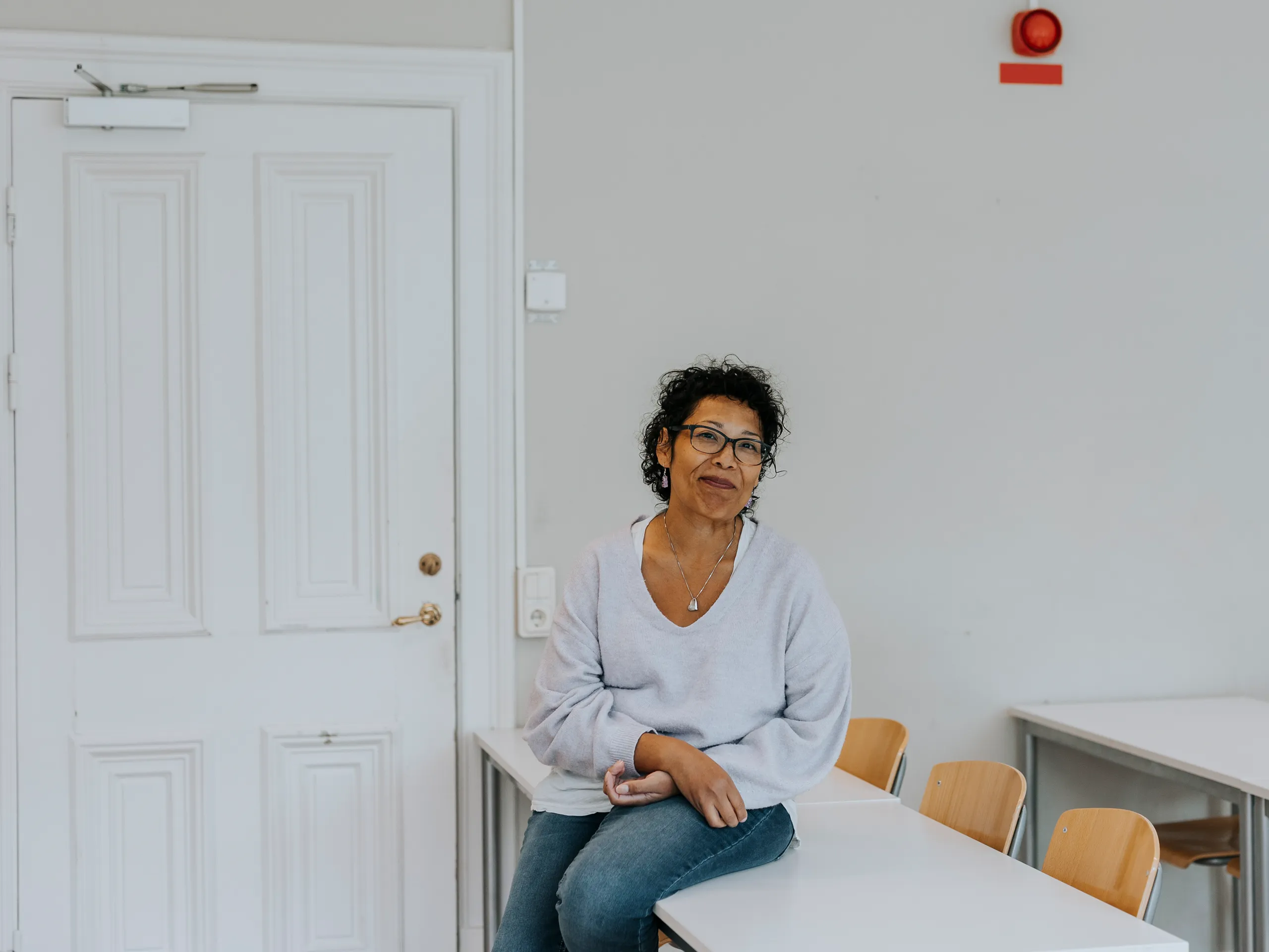 Mujer relajada con gafas sentada en una mesa blanca en un aula.