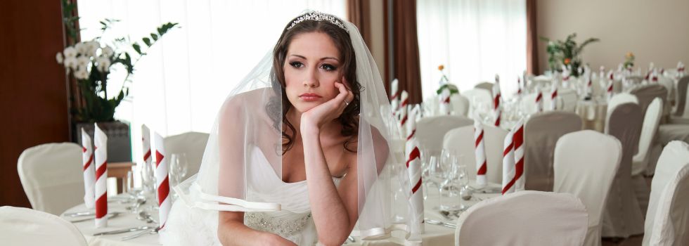 Mujer blanca vestida de novia esperando en una sala de banquetes vacía y con gesto serio