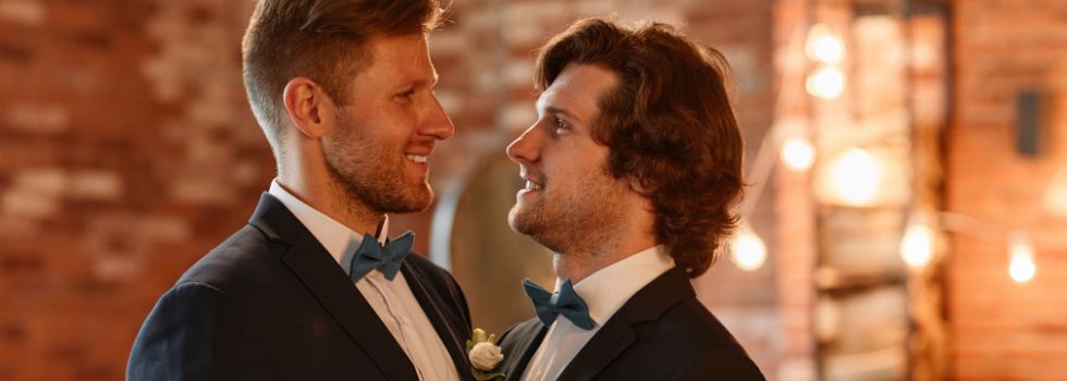 Dos hombres blancos en su boda, mirándose el uno al otro abrazados 