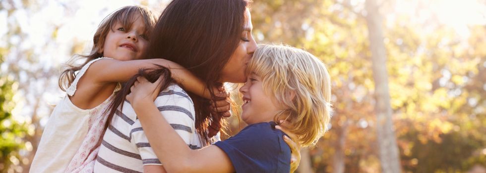 Madre blanca con hijos abrazados a ella en el exterior