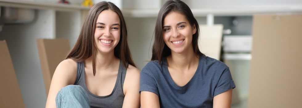 Pareja de mujeres blancas jóvenes en vivienda con cajas de mudanza al fondo