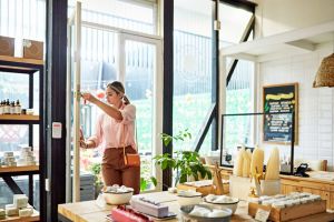 Mujer blanca abriendo la puerta de su establecimiento: una pastelería 