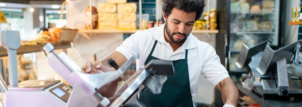 Hombre en una carnicería, cortando un trozo de carne con una máquina