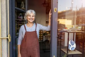 Mujer blanca senior delante de su tienda de decoración sonriendo a cámara