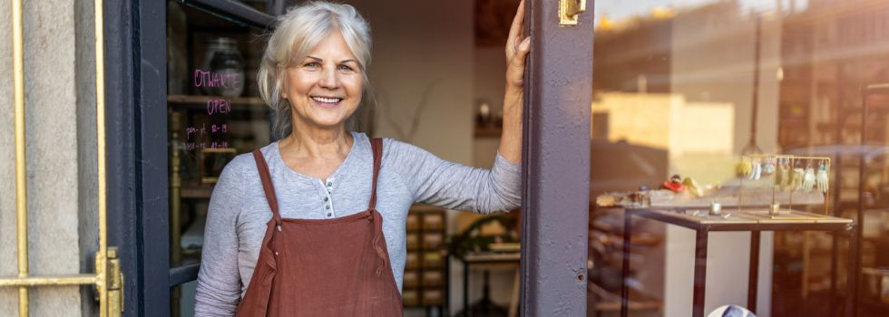 Mujer blanca senior delante de su tienda de decoración sonriendo a cámara