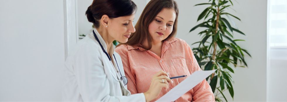 Mujer en la consulta del médico con doctora enseñándole informe médico