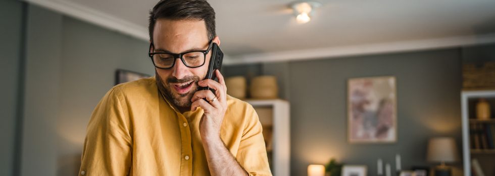 Hombre blanco con gafas hablando por teléfono y sonriendo