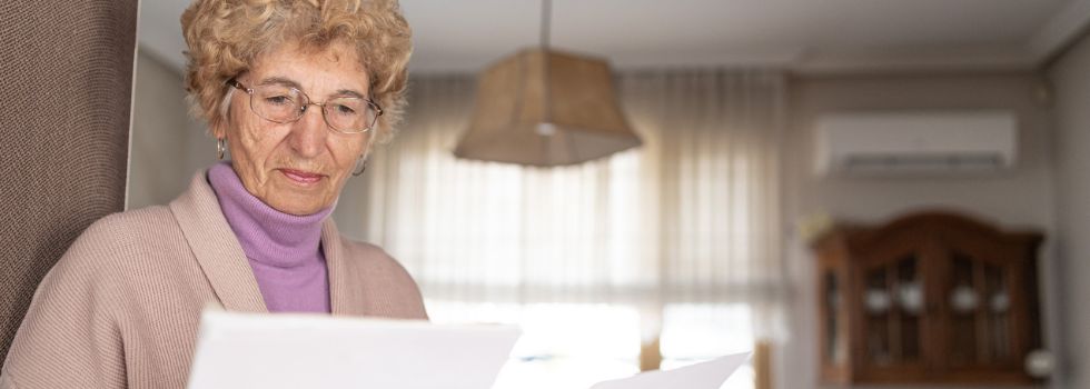 Mujer mayor blanca en su casa leyendo concentrada una carta 