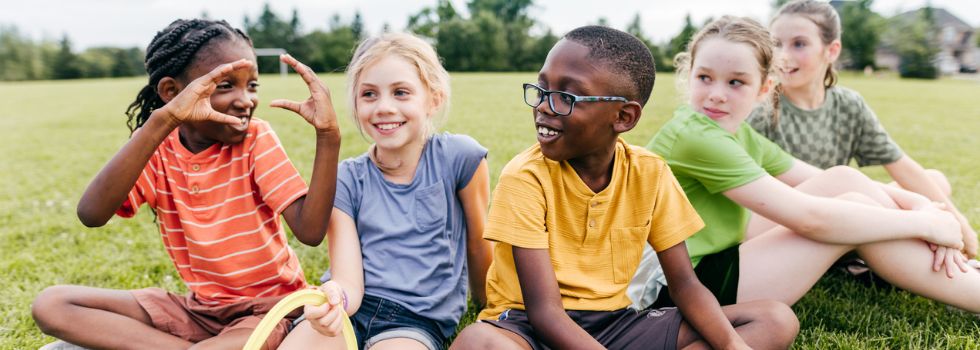 Grupo de niños multiétnicos disfrutando de un día al aire libre, sentados en el césped