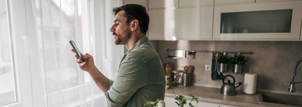 Hombre blanco en la cocina mirando su teléfono móvil