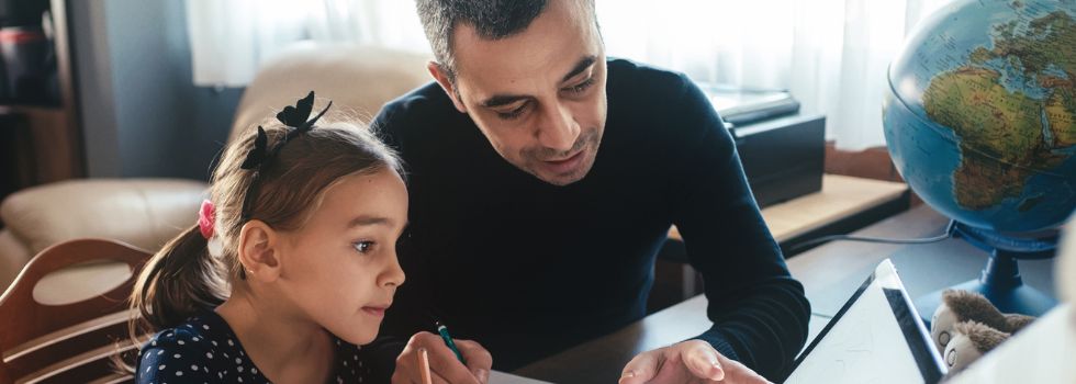 Padre con hija blancos sentados a la mesa con portátil y libro de texto