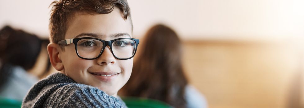Niño con gafas en clase, sonriendo y mirando a cámara