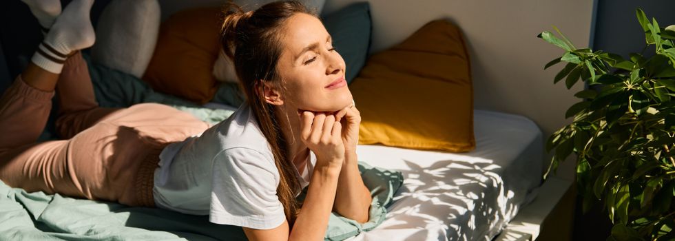 Mujer blanca disfrutando de un día brillante acostada en la cama en casa 
