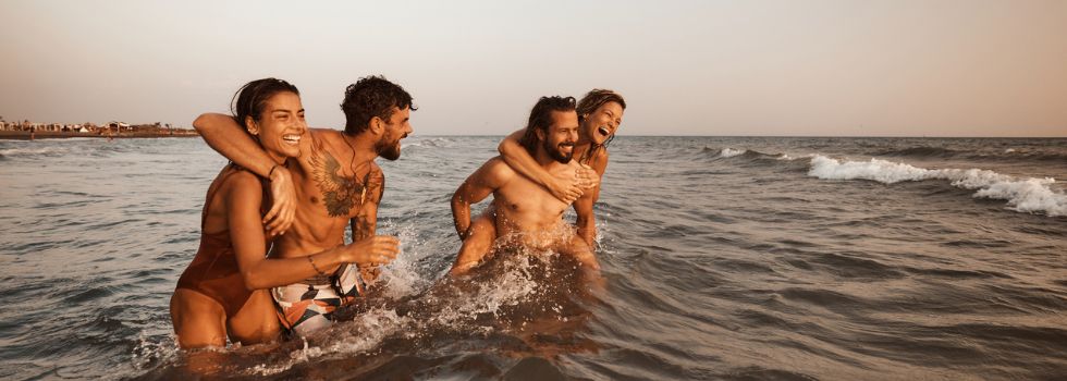 Dos chicos y dos chicas blancos y jóvenes sonrientes bañándose en el mar 