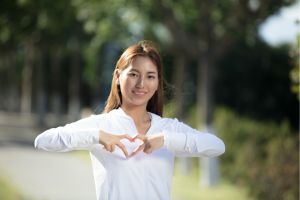 Mujer asiática en un parque haciendo un corazón con las manos