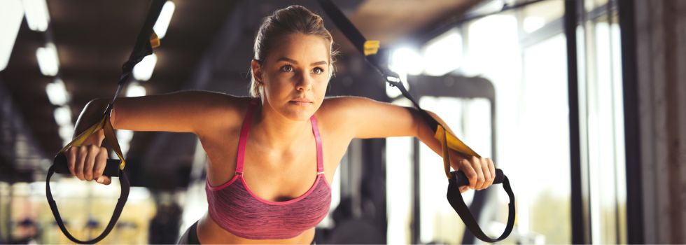 Cómo reclamar por una lesión en un gimnasio Mujer haciendo ejercicios de brazos con correas de suspensión en el gimnasio