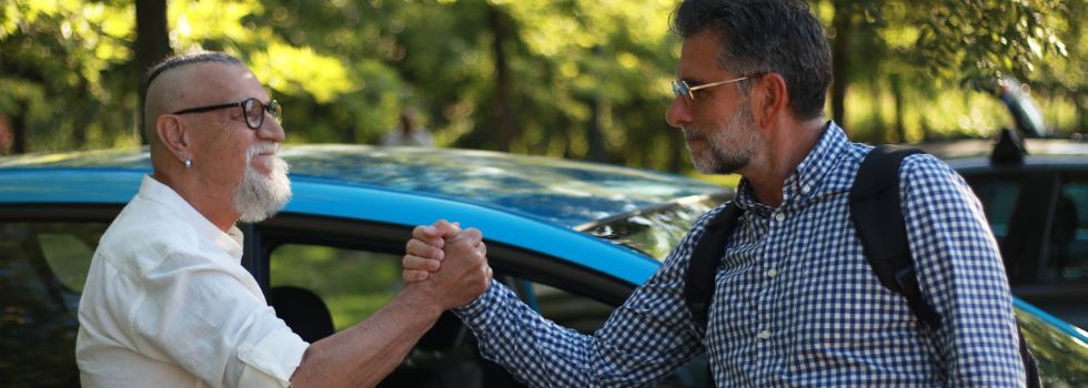 Dos hombres blancos dándose la mano, de fondo un coche. 