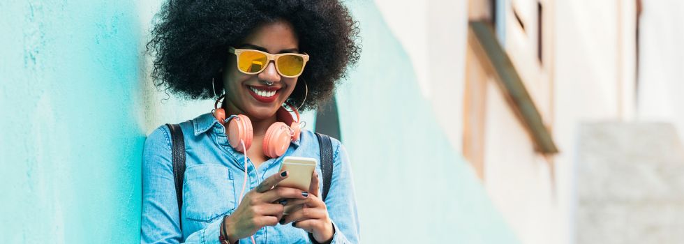 Mujer negra con afro y gafas de sol mirando el móvil en la calle