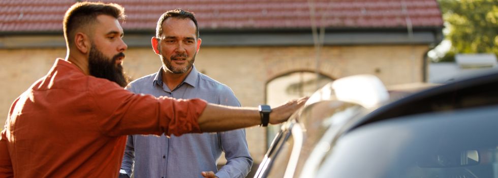 Dos hombres hablando al lado de un coche, negociando su venta