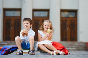 Dos niños blanco comiendo una manzana sentados encima de libros