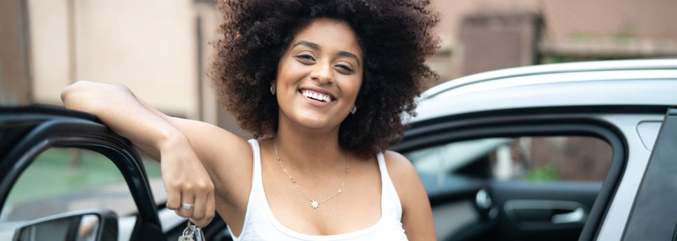 Mujer negra con pelo afro apoyada en un coche con las llaves en la mano