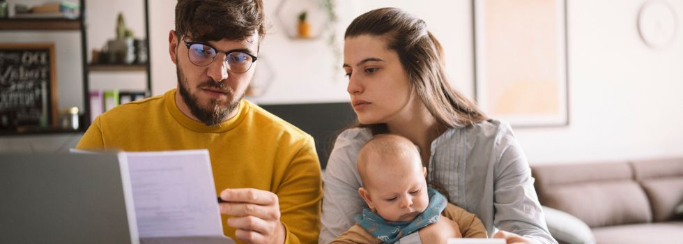 Pareja heterosexual con su bebé revisando facturas sentados a la mesa