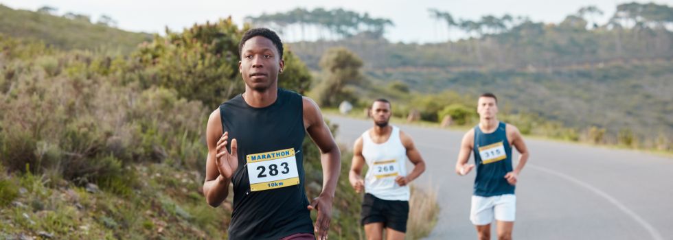 Tres hombres con dorsal corriendo por una carretera, con uno de ellos en cabeza