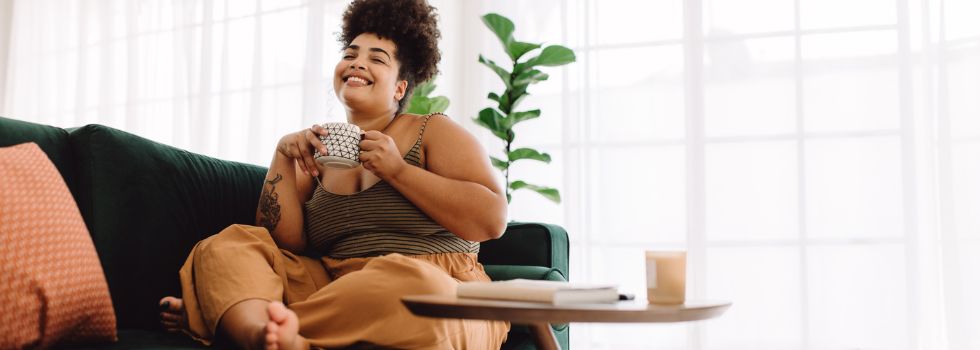 Mujer de talla grande sentada en el sofá, sonriendo y tomando un café