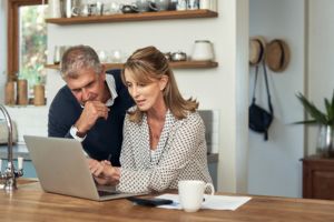 Hombre y mujer blancos mirando el portátil en su cocina