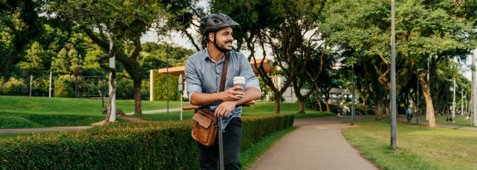 Hombre joven blanco montado en patinete eléctrico por un parque