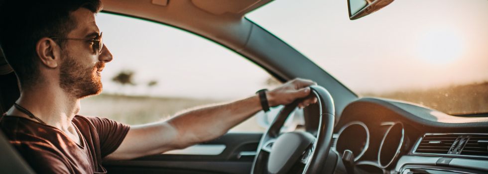 Hombre con gafas de sol al volante, conduciendo al atardecer