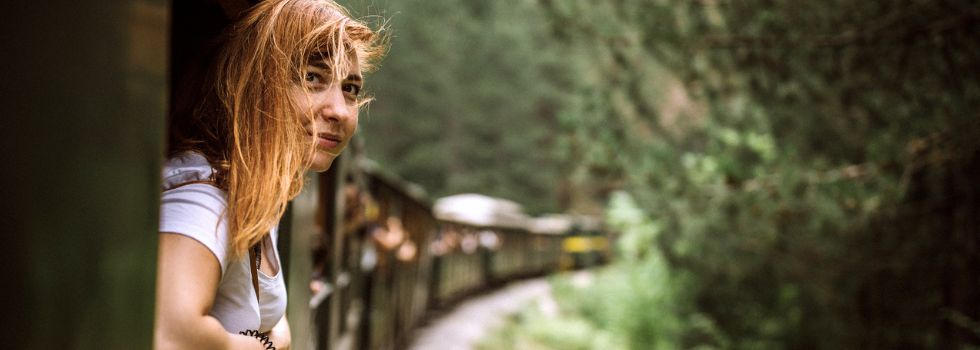 Mujer blanca asomada a la ventana de un tren en movimiento que pasa por un bosque
