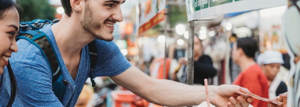 Pareja de hombre blanco y mujer asiática de viaje, comprando bebida de coco en un mercado callejero