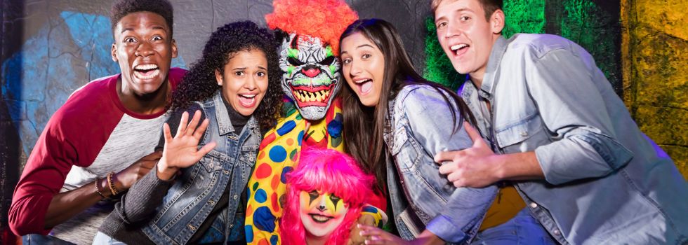 ¿Cuáles son los mejores parques temáticos de terror? Grupo multiétnico haciéndose una foto en un parque de terror con un payaso macabro