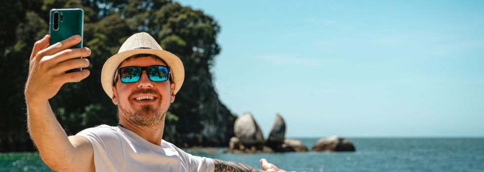 Hombre caucásico tomando una selfie con teléfono inteligente en Split Apple Rock, Parque Nacional Abel Tasman, Nueva Zelanda